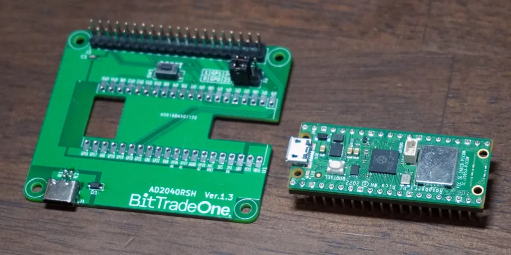 BitTradeOne AD2040RSH Ver 1.3 development board with long 40-pin header beside a Raspberry Pi Pico–style microcontroller board on a wooden surface