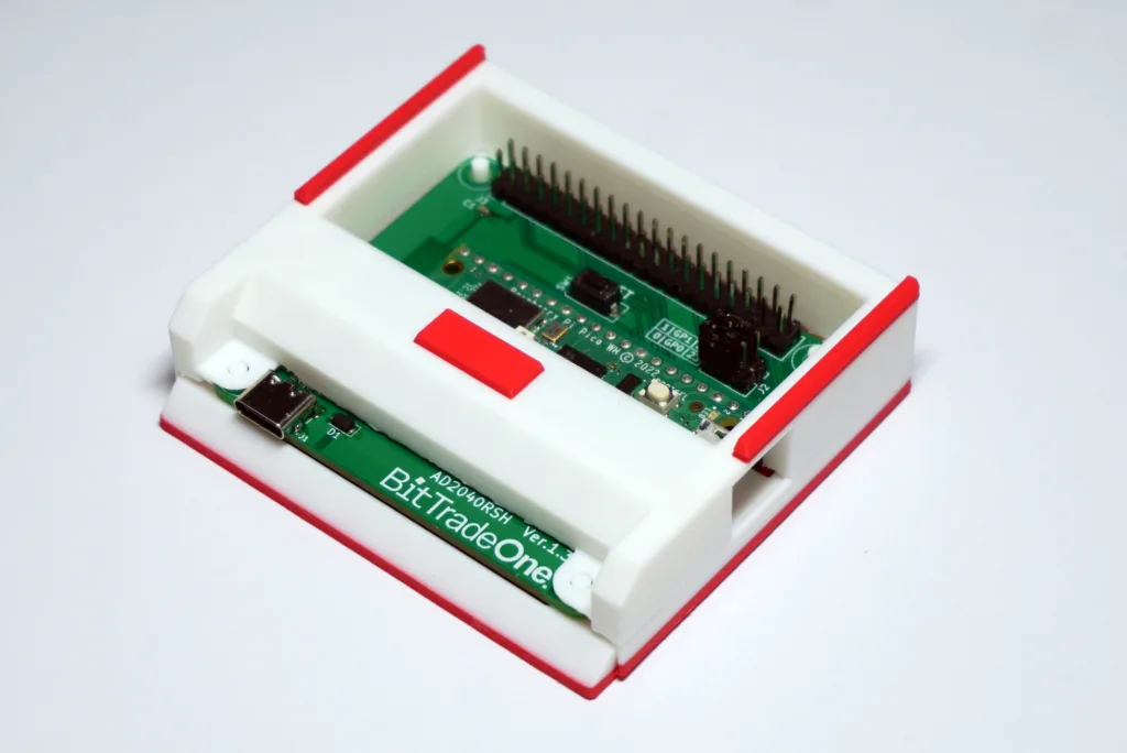 Close-up of a green PCB with many header pins inside a white plastic case with red trim on the edges.