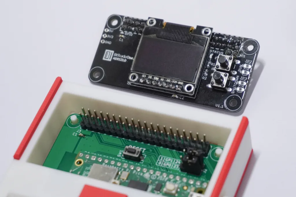 Close-up of a black module with a grid of pins mounted on a green development board inside a white/red plastic enclosure, showing exposed headers and connectors.