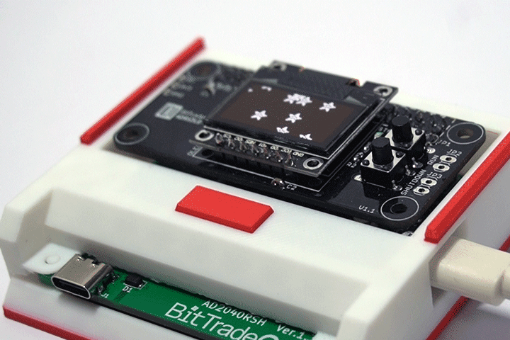Microcontroller development board on a white plastic chassis with red rails; a green BitTrade breakout board is connected via USB-C.