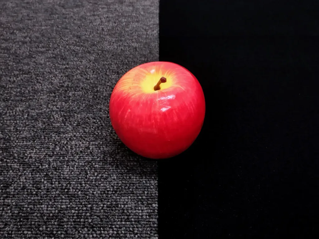Red apple resting on a two-tone surface: gray carpet on the left and black fabric on the right.