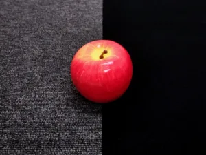 Red apple resting on a two-tone surface: gray carpet on the left and black fabric on the right.