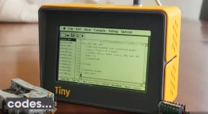 Yellow retro handheld computer displaying a green text editor with code on its screen.