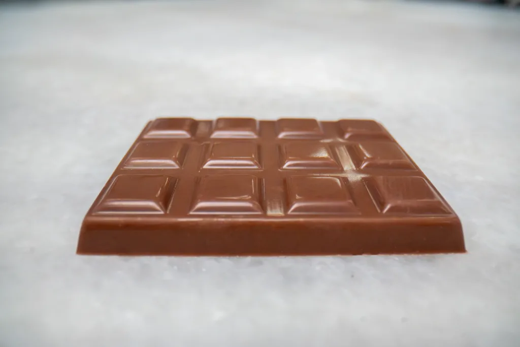 Milk chocolate bar lying flat on a pale marble surface, viewed from a low angle.