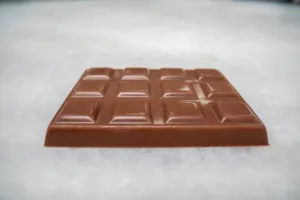Milk chocolate bar lying flat on a pale marble surface, viewed from a low angle.