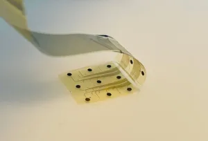 Close-up of a pale, perforated adhesive tape strip bent on a light surface.