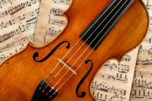 Close-up of a violin resting on scattered sheet music, showing the f-holes and strings against a warm wooden body.