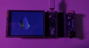 Raspberry Pi Pico microcontroller board connected to a small LCD display, photographed in purple lighting with a blue screen showing a vague shape.