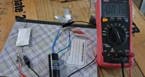 Pink digital multimeter with probes connected to a circuit on a wooden workbench, surrounded by wires and components (capacitor, clips). Rea­ding visible on display is 0.58.