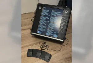 Portable karaoke/lyrics display in a rugged case on a wooden floor, screen showing German lyrics and a three-foot pedal accessory nearby.
