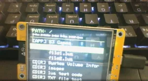 Yellow OLED display mounted on a PCB showing terminal-style text (PATH: and commands) with a backlit keyboard in the background.
