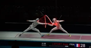 Two fencers in white gear duel on a strip; red digital graphics highlight the target area around one fencer's torso during the lunge.