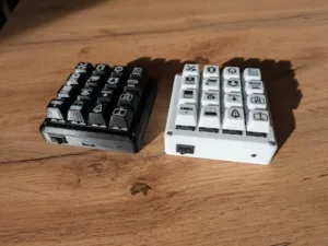 Two compact mechanical keyboards with square icon-keycaps, black on the left and white on the right, on a wooden desk.