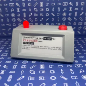 Gray handheld device with two red top buttons; its display shows "Word of the Day" for 13-Apr, listing "KIBITZER noun" and a short definition.