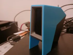 Blue 3D-printed heatsink or cooling block with vertical black fins on a desk, cables in the background