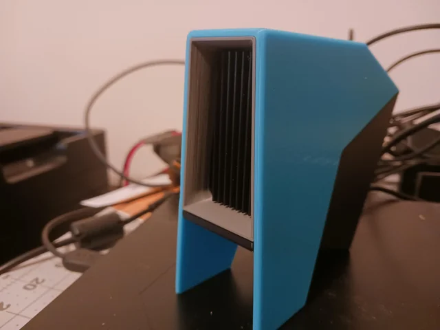 Blue 3D-printed heatsink or cooling block with vertical black fins on a desk, cables in the background