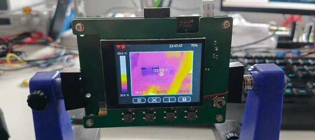 Thermal camera module on a lab stand, displaying a color temperature image on a small screen.