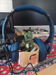 Blue over-ear headphones encircle a green circuit board mounted between the earcups.
