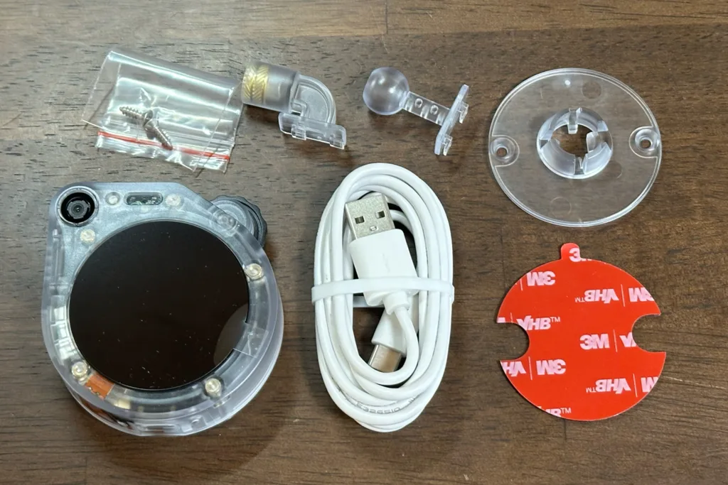 Round transparent camera housing with black lens, plus USB cable and mounting hardware set on a wooden surface.