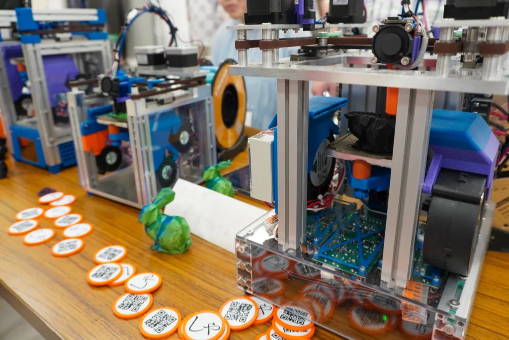 Row of orange circular tokens with QR codes on a wooden table in a robotics lab scene.