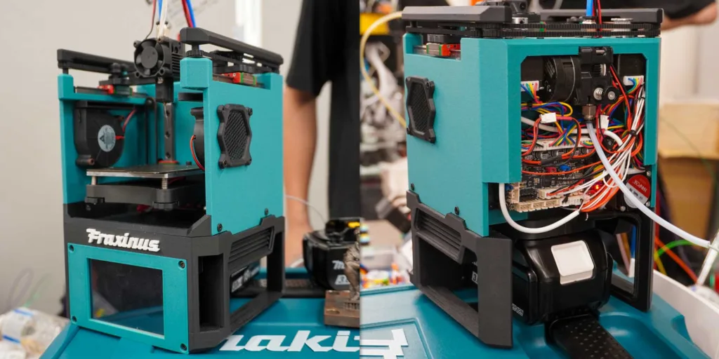 Two teal desktop 3D printers with open frames and exposed wiring on a workshop table.