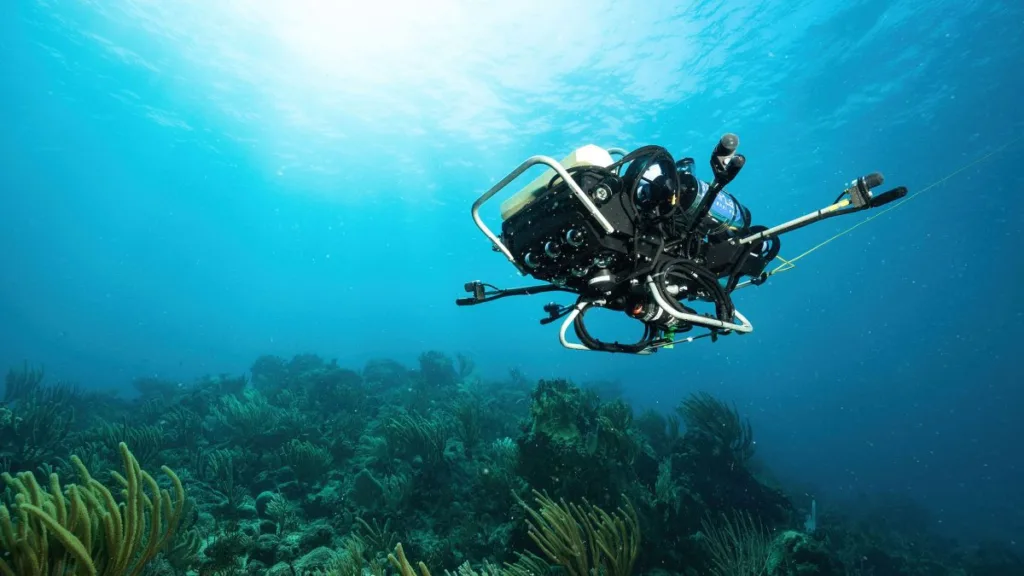 Underwater drone with cameras exploring a coral reef, blue ocean surrounding it.