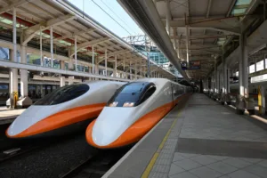 Two white and orange high-speed trains on a modern station platform with steel framework overhead and clear glass canopies.