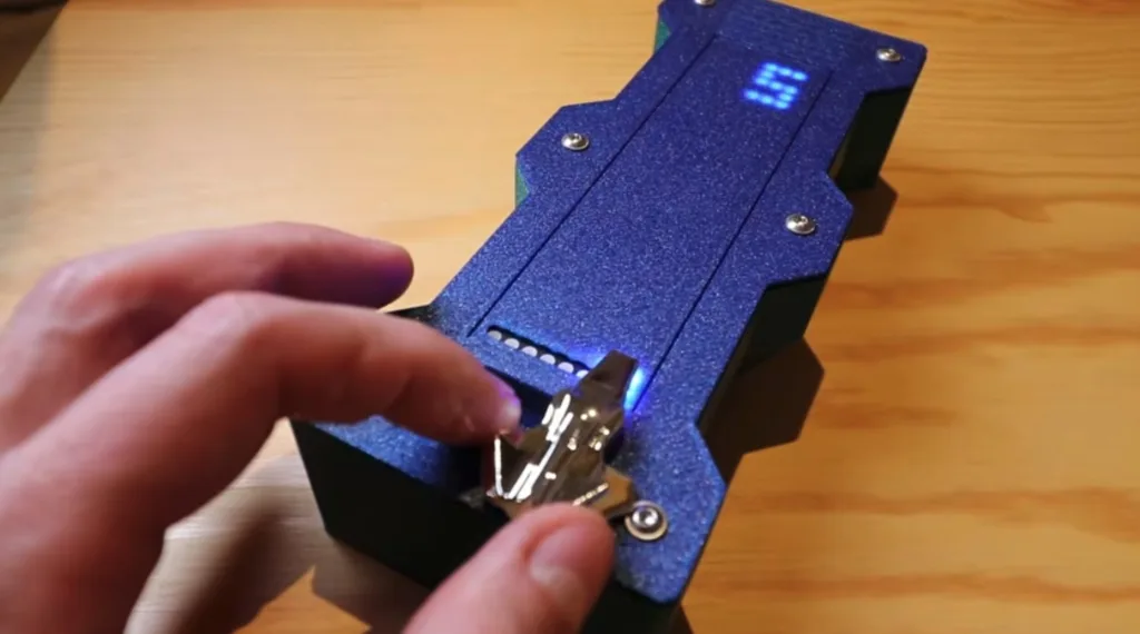 Person attaching a small circuit board to a blue textured device with a glowing blue LED display on top.