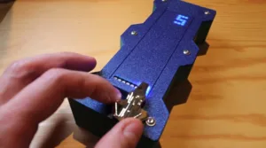 Person attaching a small circuit board to a blue textured device with a glowing blue LED display on top.