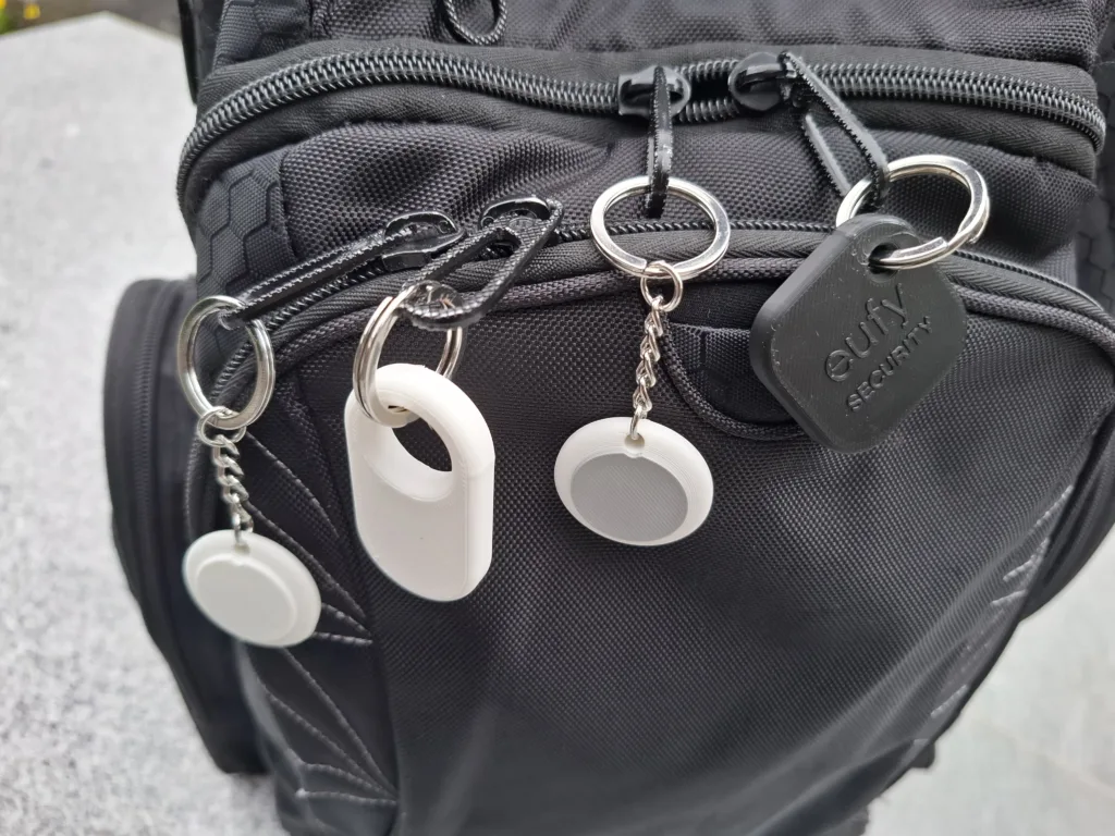 Close-up of a black backpack with multiple zippers, metal rings, and white circular tags attached to the front.