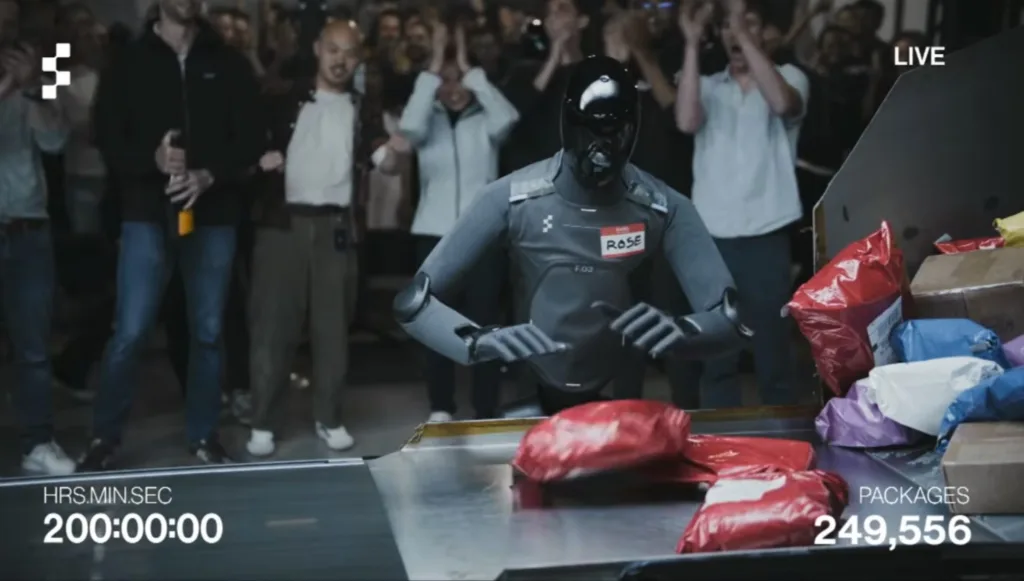 Robot in a gray suit and black helmet stands at a packaging station while a cheering crowd watches; live overlay and numbers on screen show time and packages.