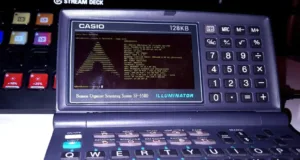 Casio handheld calculator with a terminal screen showing ASCII art and system info, labeled ILLUMINATOR on the bottom edge.