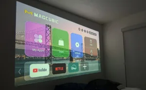 Projector showing a home screen with app icons (My Apps, Store, Settings) on a wall above a bridge image backdrop, including YouTube, Netflix, and Disney+ icons.