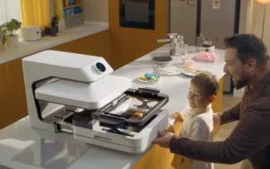 Father and young child stand at a kitchen island watching a white multifunction printer print.
