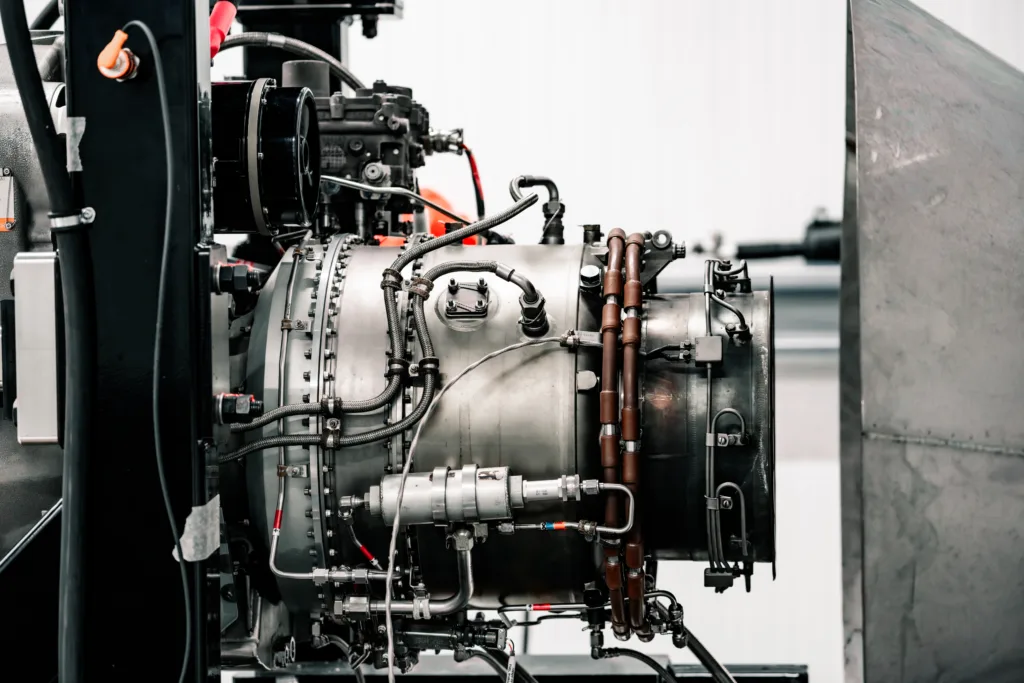 Close-up of a complex industrial engine with numerous pipes, hoses, and metal fittings inside a machinery housing.
