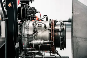 Close-up of a complex industrial engine with numerous pipes, hoses, and metal fittings inside a machinery housing.