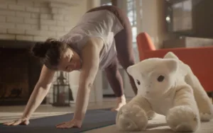 Person on hands and knees in a yoga pose on a mat in a living room, with a large white plush animal nearby.