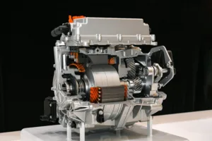 Cutaway model of a metallic engine showing gears and orange wiring on a white stand against a dark background.