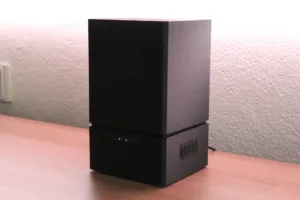 Two stacked black computer towers with vented front panels on a wooden desk, blue indicator lights glowing.
