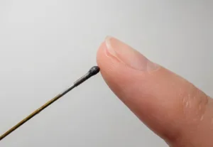 Close-up of a small precision brush touching the tip of a fingernail, held near the nail bed