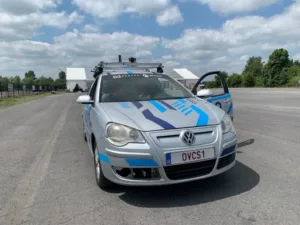 Silver VW station wagon with blue geometric decals parked on an empty tarmac, driver door open under a cloudy sky.