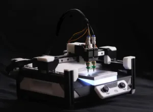 Desktop CNC engraver with dual tool heads and visible wiring, set against a dark background.