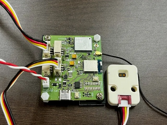 Green circuit board with multiple connectors and red, yellow, black wires attached, on a wooden surface.