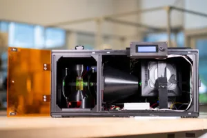Industrial equipment with an orange hinged door open, revealing internal components and wiring inside a metal frame.