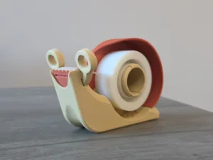 Beige plastic desktop tape dispenser with a red guard and a roll of clear tape on a gray wooden surface.