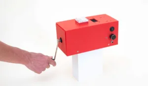 Red handheld-powered machine on a white stand, being operated with a wrench-style crank handle