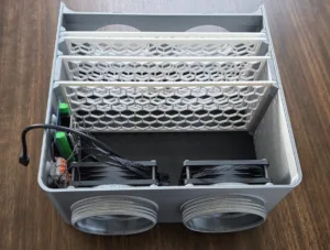 Interior view of a compact metal computer chassis with three white honeycomb vent panels, two large circular front fans, and tangled cables with green terminal blocks.