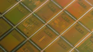 Close-up of a silicon microchip with green and orange rectangular circuit blocks and silver interconnects in a diagonal grid pattern.