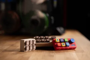 Close-up of two small toy keyboards with gray and colored buttons on a wooden table, blurred background.