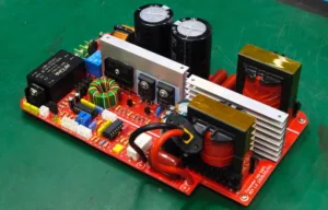 Red power electronics board with large capacitors, inductors, transformers and connectors on a green work surface